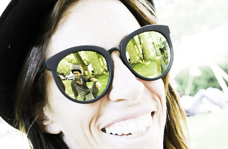 A woman wearing sunglasses and a hat is smiling.