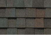 Close-up of overlapping asphalt roof shingles in shades of brown, green, and gray.