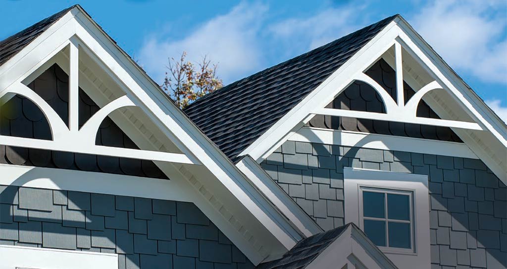 Exterior of a blue-gray house with white trim, dark roof, and decorative arched gable accents.