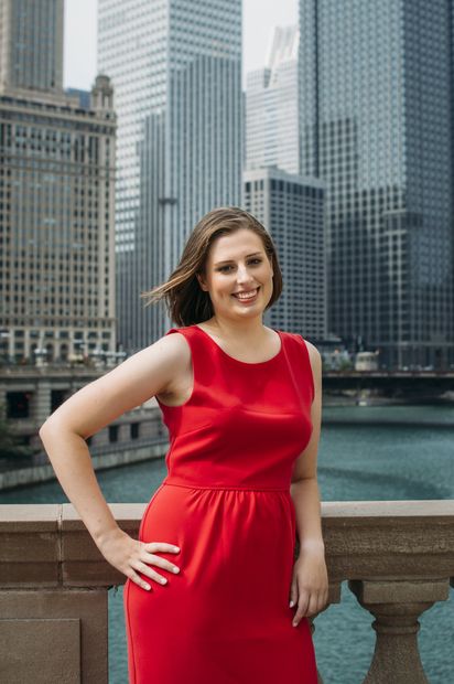 A woman in a red dress is standing on a bridge in front of a city skyline.