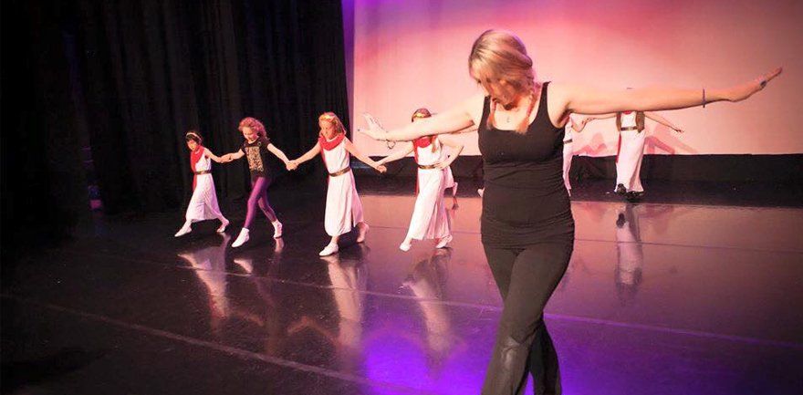 teacher leading a bow on stage with dancers behind her