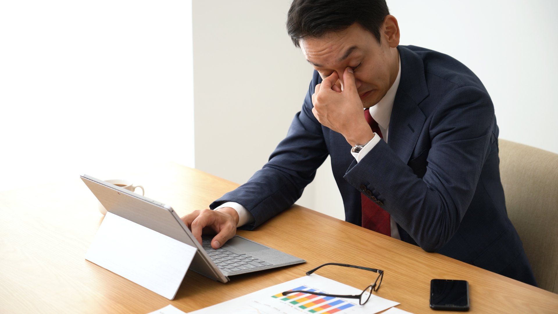 A man in a suit and tie is sitting at a desk using a laptop computer.