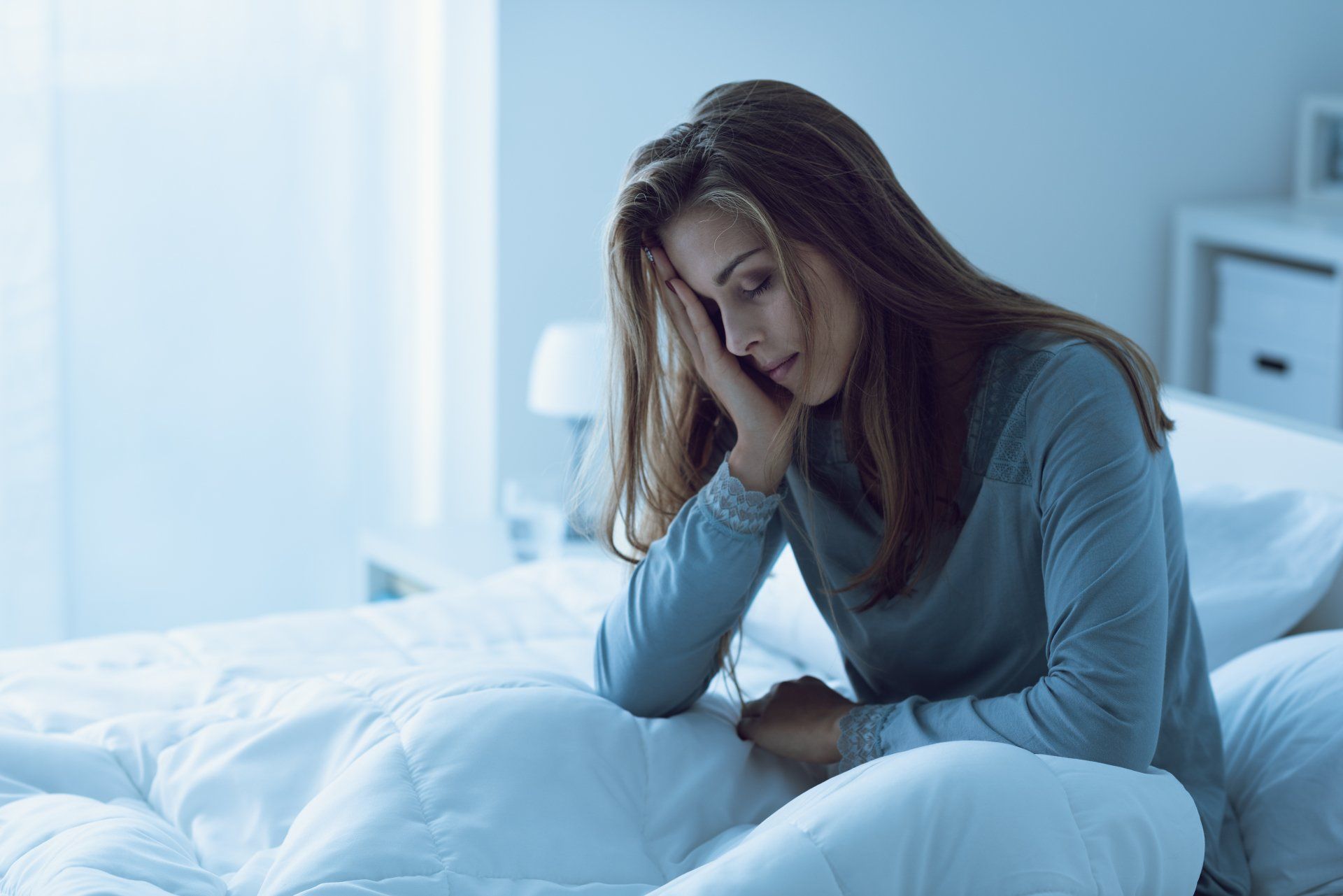 A woman is sitting on a bed with her head in her hands.
