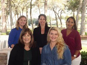 A group of women are posing for a picture in front of trees.