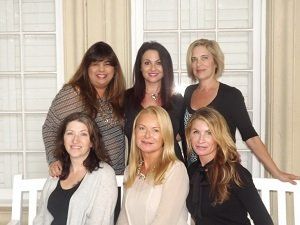 A group of women are posing for a picture in front of a window.
