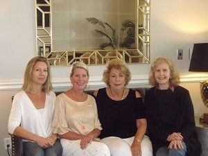 Four women are sitting on a couch in front of a mirror.