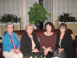 Four women are posing for a picture while sitting on a couch.