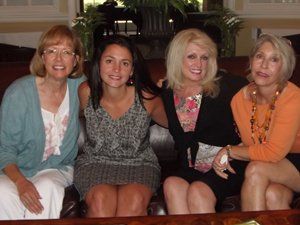 Four women are posing for a picture while sitting on a couch.