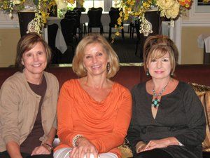 Three women are posing for a picture while sitting on a couch.