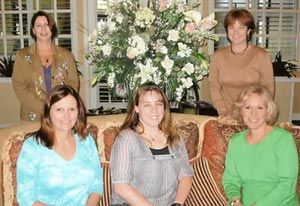 Four women are posing for a picture in front of a vase of flowers