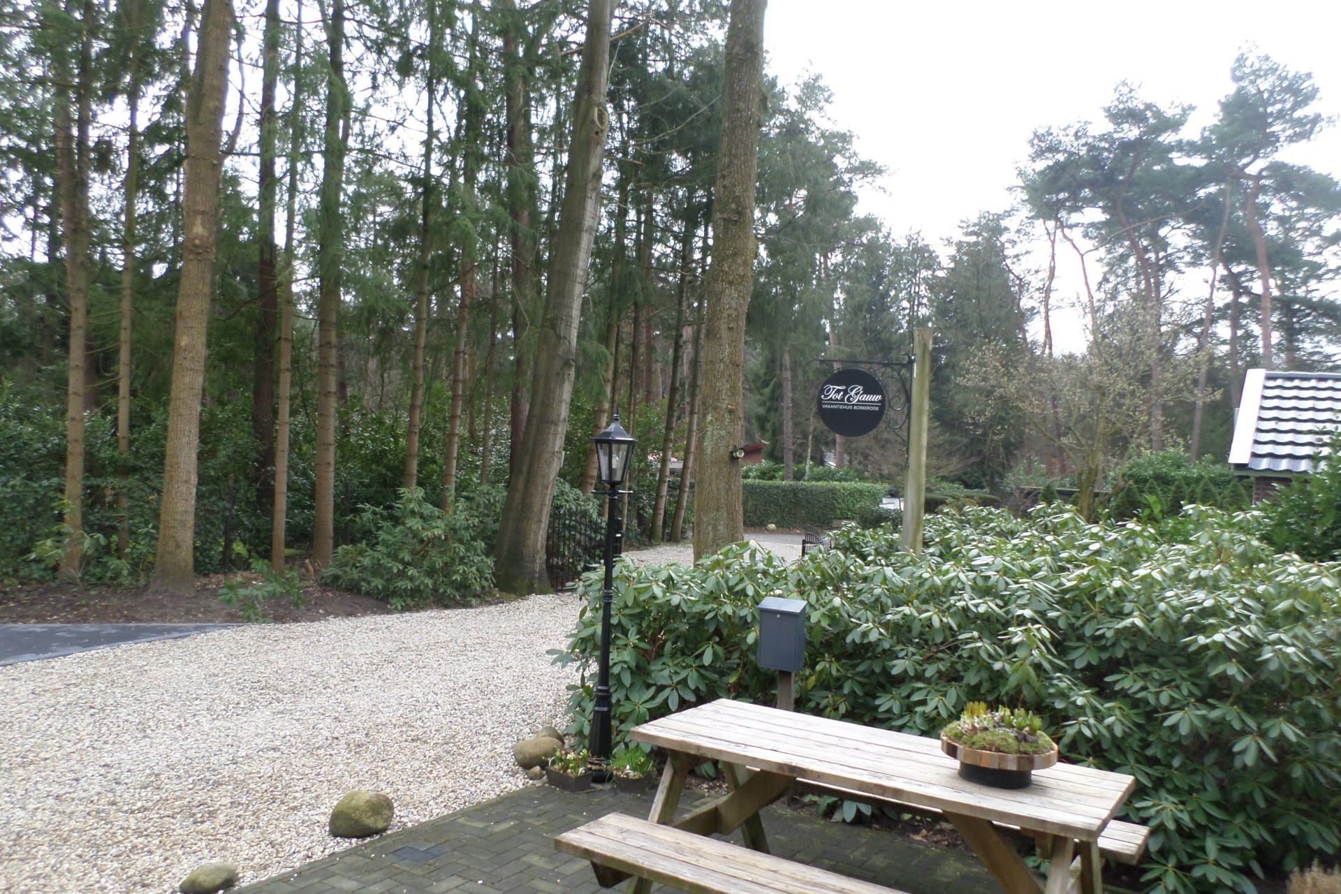 Een grindpad leidt naar een bosrijk gebied met een picknicktafel en een bord. Bewolkte lucht.