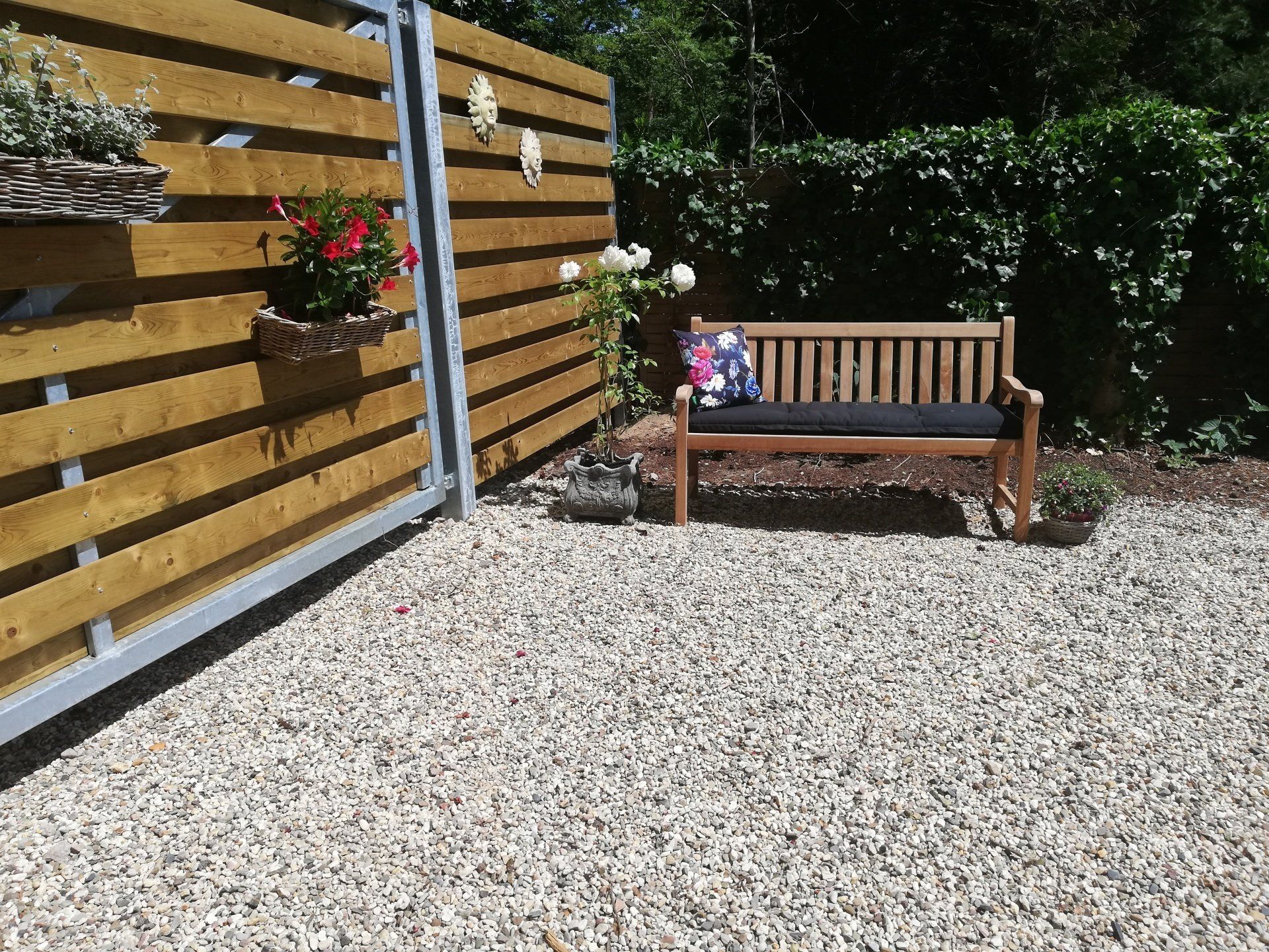 Houten bank op grind naast een horizontale houten schutting met bloemen.