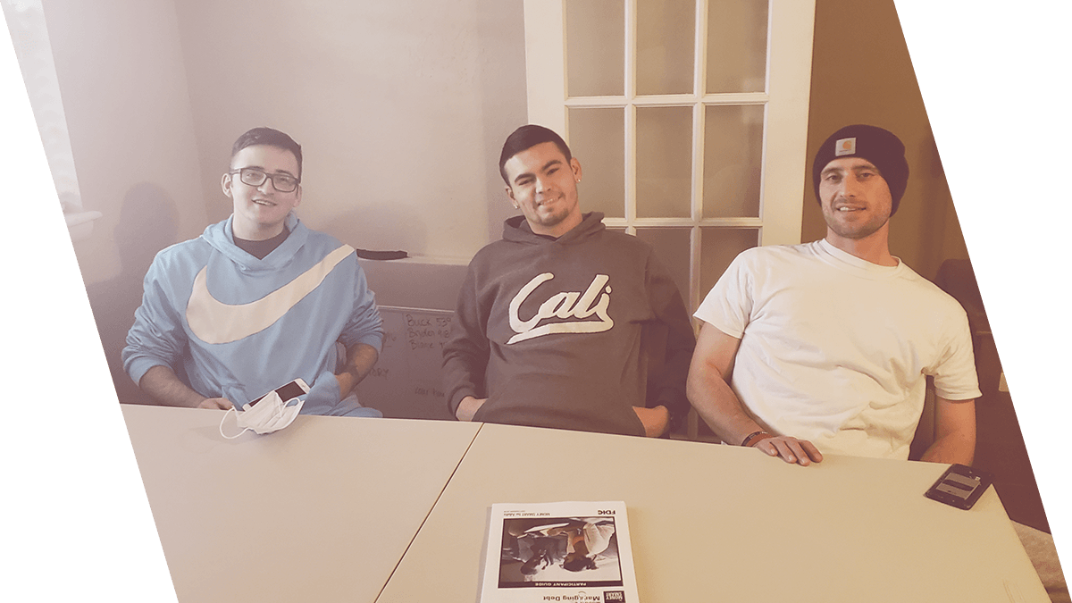 Three men are sitting at a table with a magazine on it.