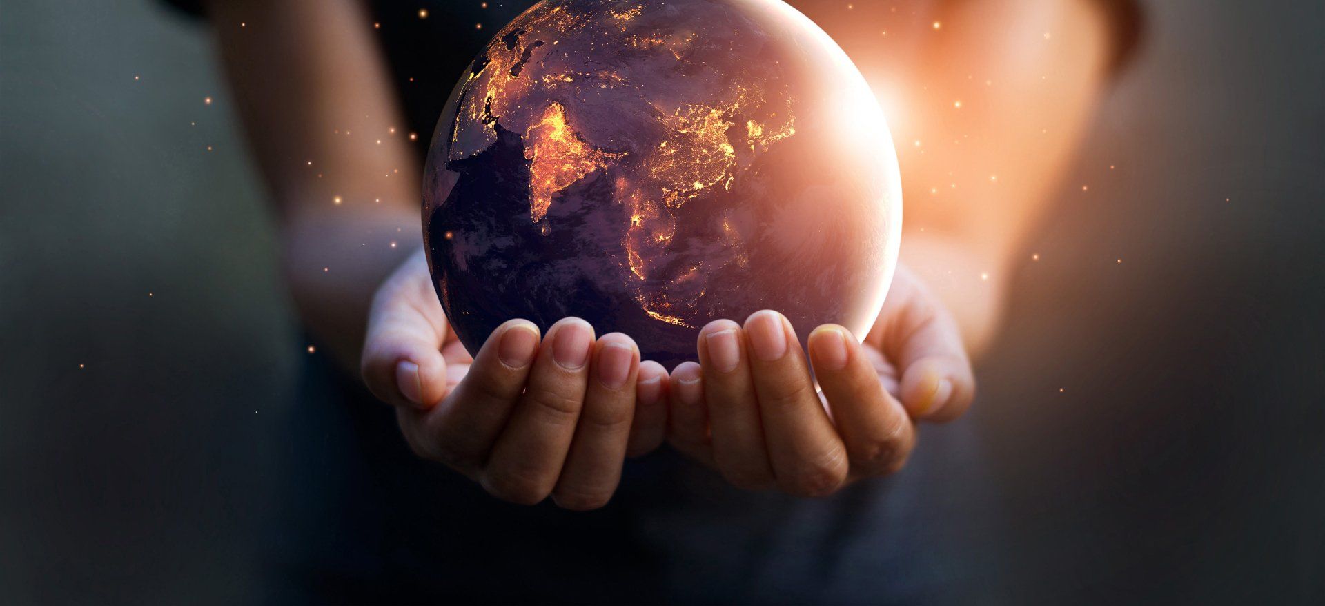 Stock picture of a person holding a globe of the world. The globe is lit up with city lights at night.
