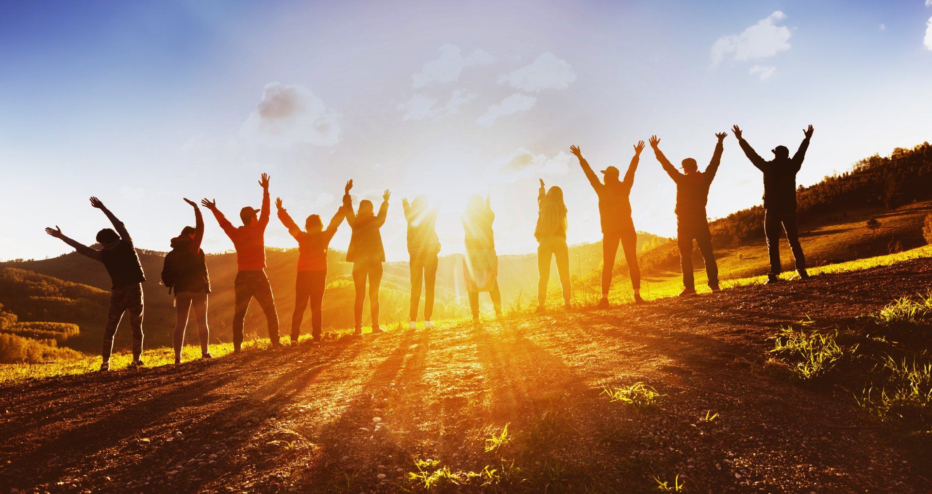 Stock picture of people standing in a field, raising their arms, silhouetted against the morning sun