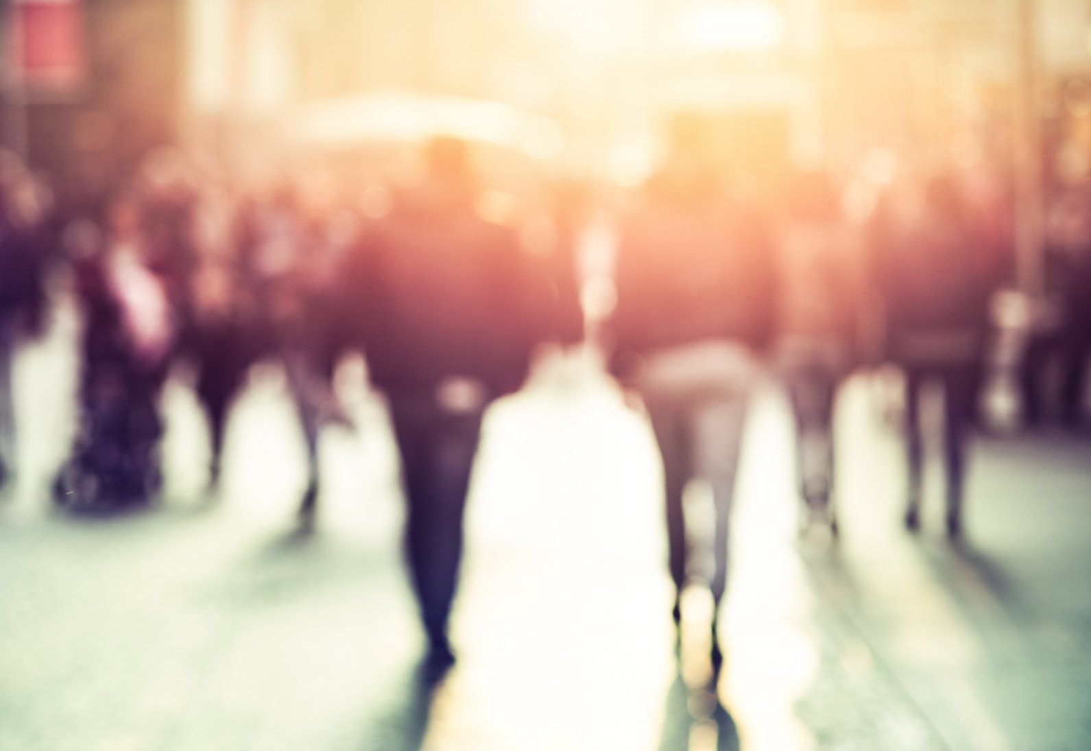 Stock picture of a street crowd walking away from the viewer. The picture is blurry and lit from above