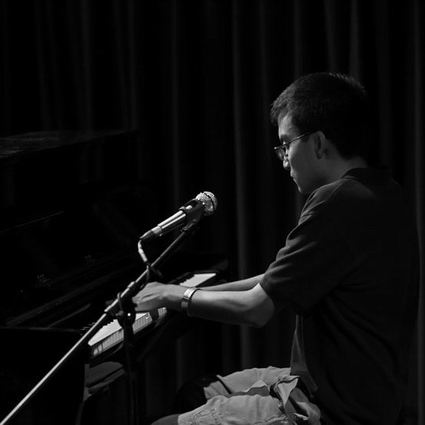 Man playing piano, facing left, in dim lighting. Black and white photo.