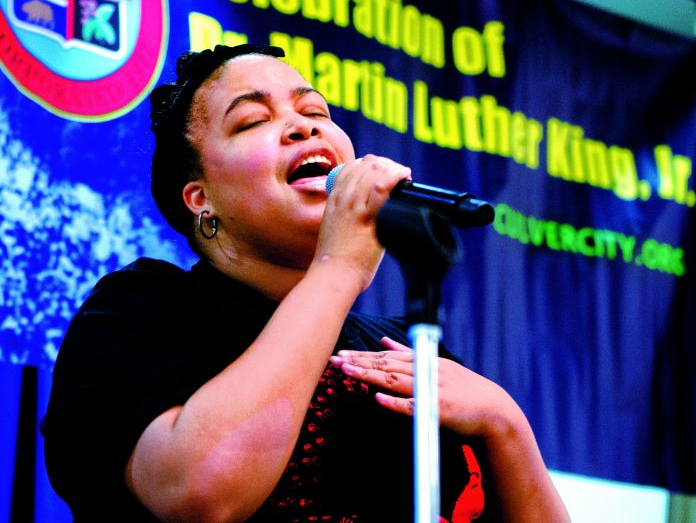 Woman singing into a microphone with her hand on her chest during Dr. Martin Luther King Jr. celebration.