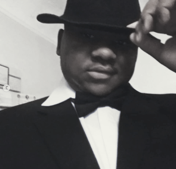 Man in tuxedo, black hat, bow tie, indoors, smiling.