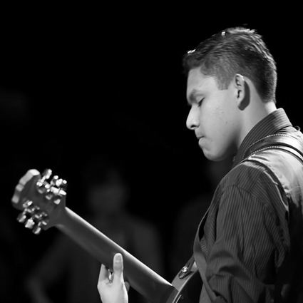 Man playing guitar, side view, focused expression, in dim setting.