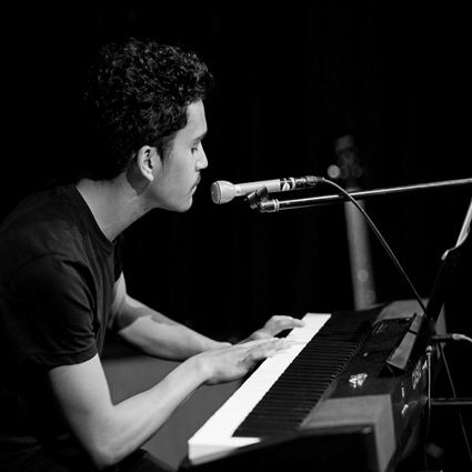 Man singing and playing a keyboard in a dimly lit setting.