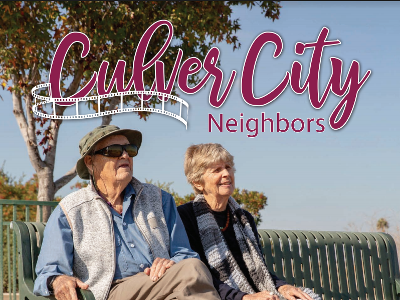 Older couple sits on park bench in Culver City, CA. Sunny day, blue sky.