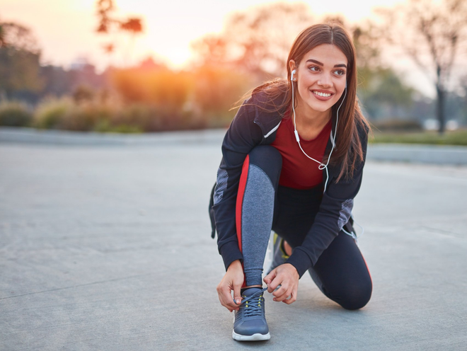 Young modern woman tying running shoes in urban park.