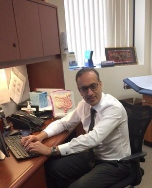 Man in office, typing on keyboard. He's wearing glasses, a white shirt, and tie. A model of intestines sits on the desk.