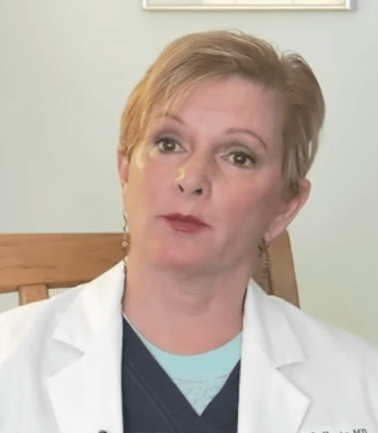 A woman wearing a white lab coat and a blue scrub is sitting in a chair