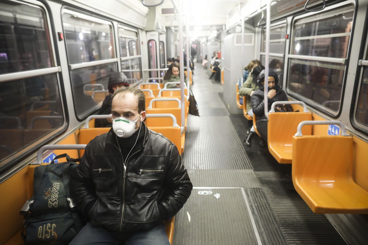 A man wearing a mask sits alone on a nearly empty metro car during the pandemic.