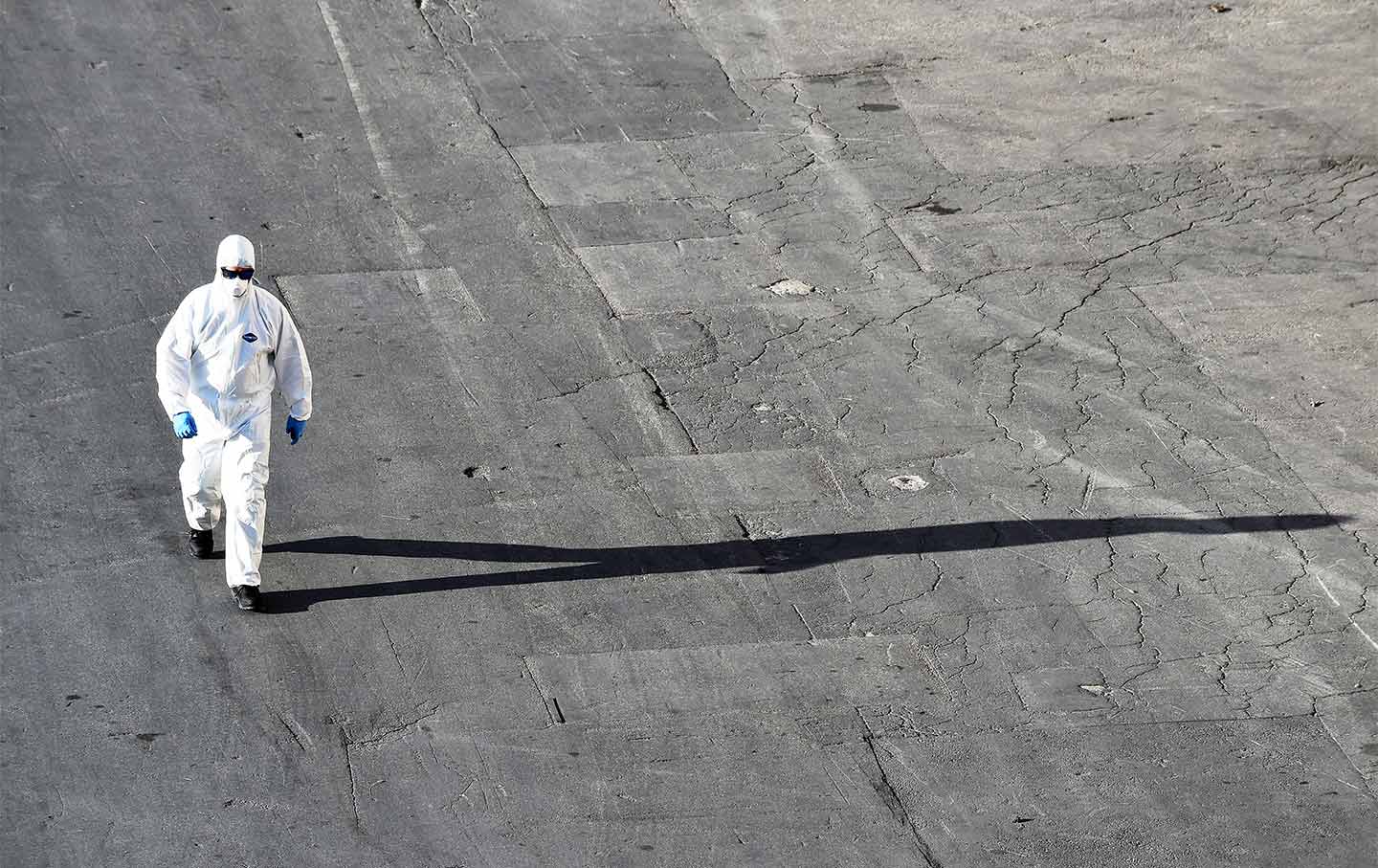 An infectious disease team member wearing a white hazmat suit walking along the pavement.