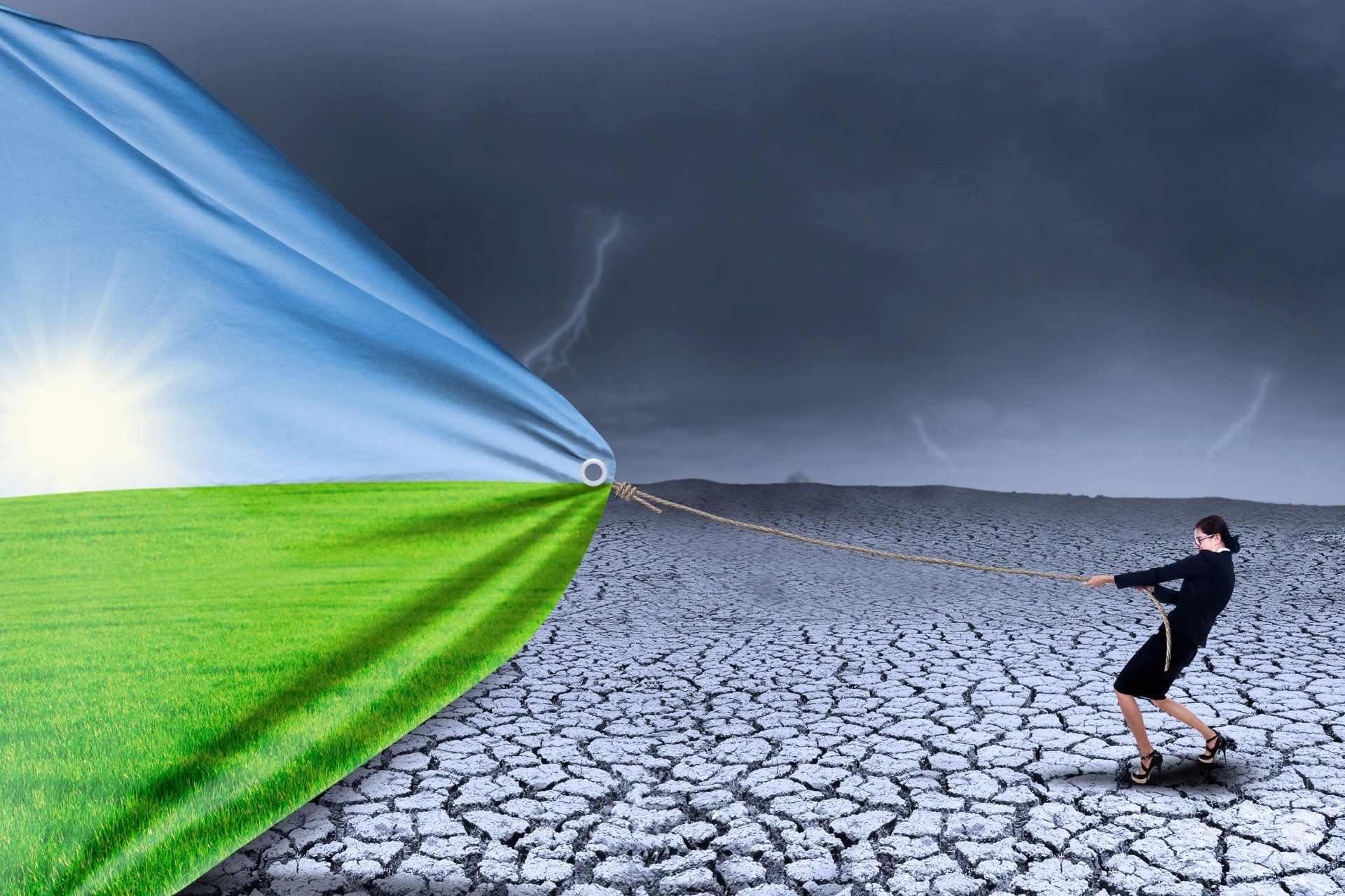A businesswoman standing on grey, cracked earth and pulling a bright and beautiful day closer to her