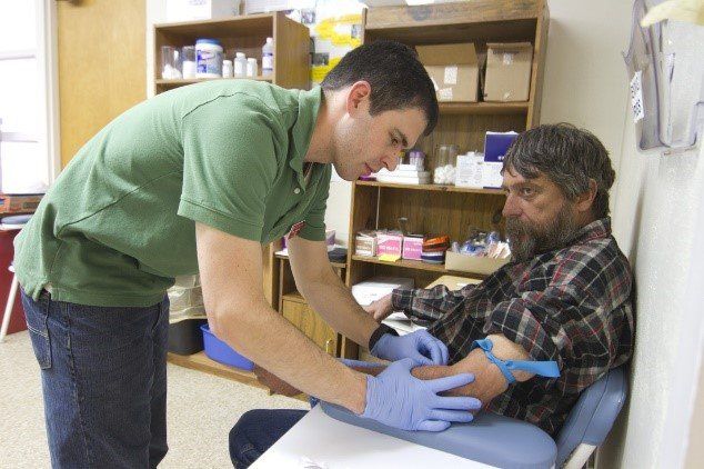 A male clinic worker prepares a patient to get his blood drawn.