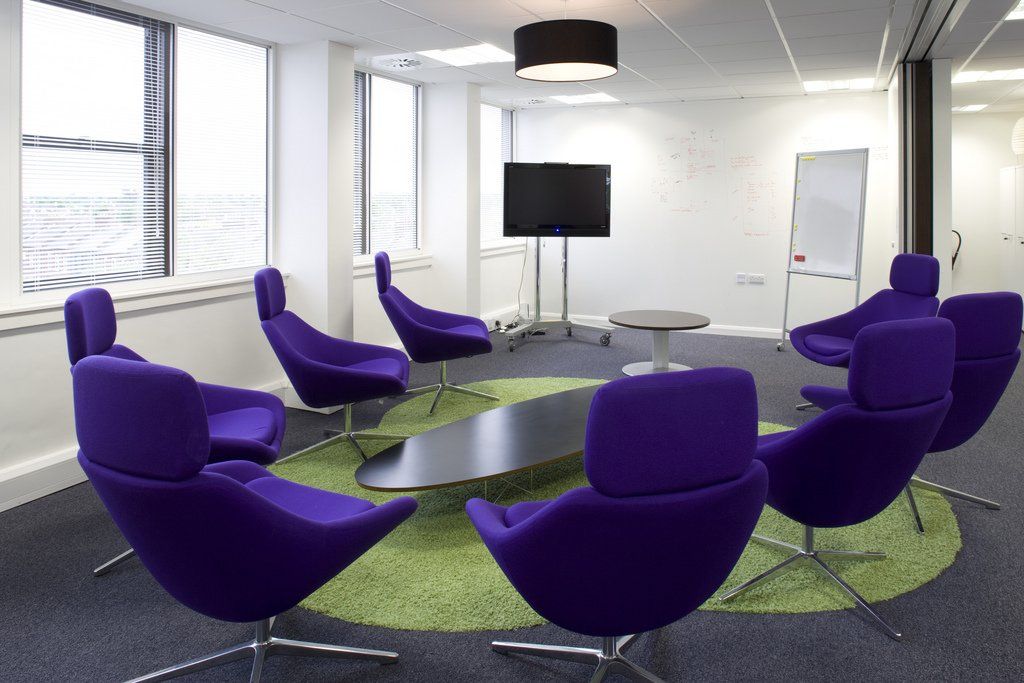 Eight purple chairs surround a table in a modern conference room.
