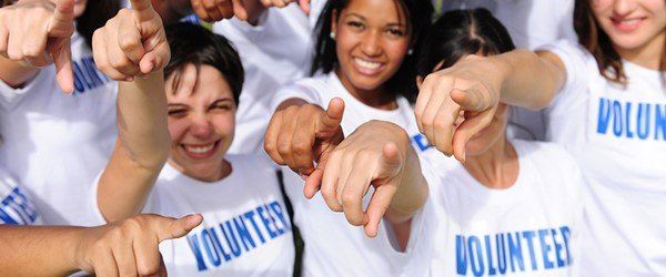 A group of volunteers smiel and point towards the camera
