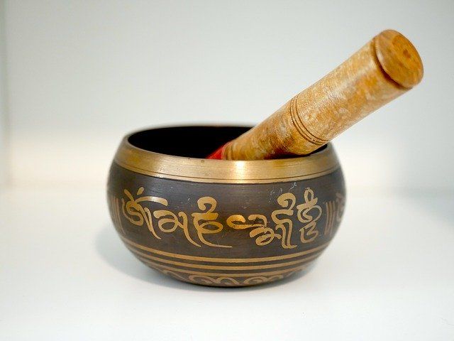 Tibetaanse klankschaal met houten stokje, gouden opschrift, staand op een witte ondergrond.