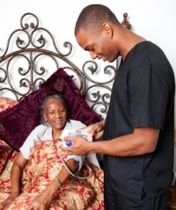 Man in black shirt checks an elderly woman's blood pressure in bed with a decorative headboard
