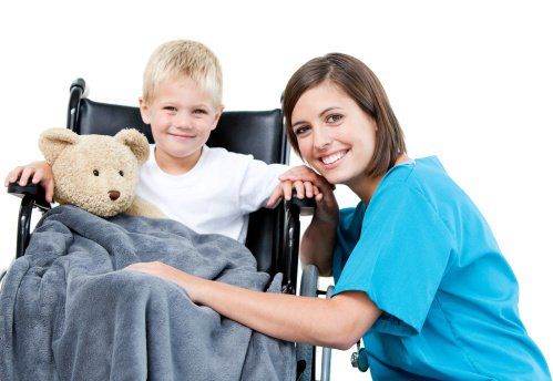 Smiling child with teddy bear in wheelchair beside a woman in blue