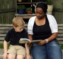 Two people sit on outdoor steps reading a book together.