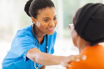 Nurse in blue scrubs smiling and speaking to a patient in an orange shirt