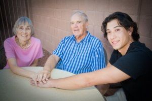 Three people smiling at a table, holding hands in a bright room
