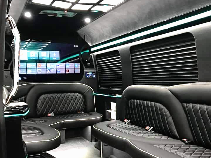 The inside of a van with black leather seats and a large screen.