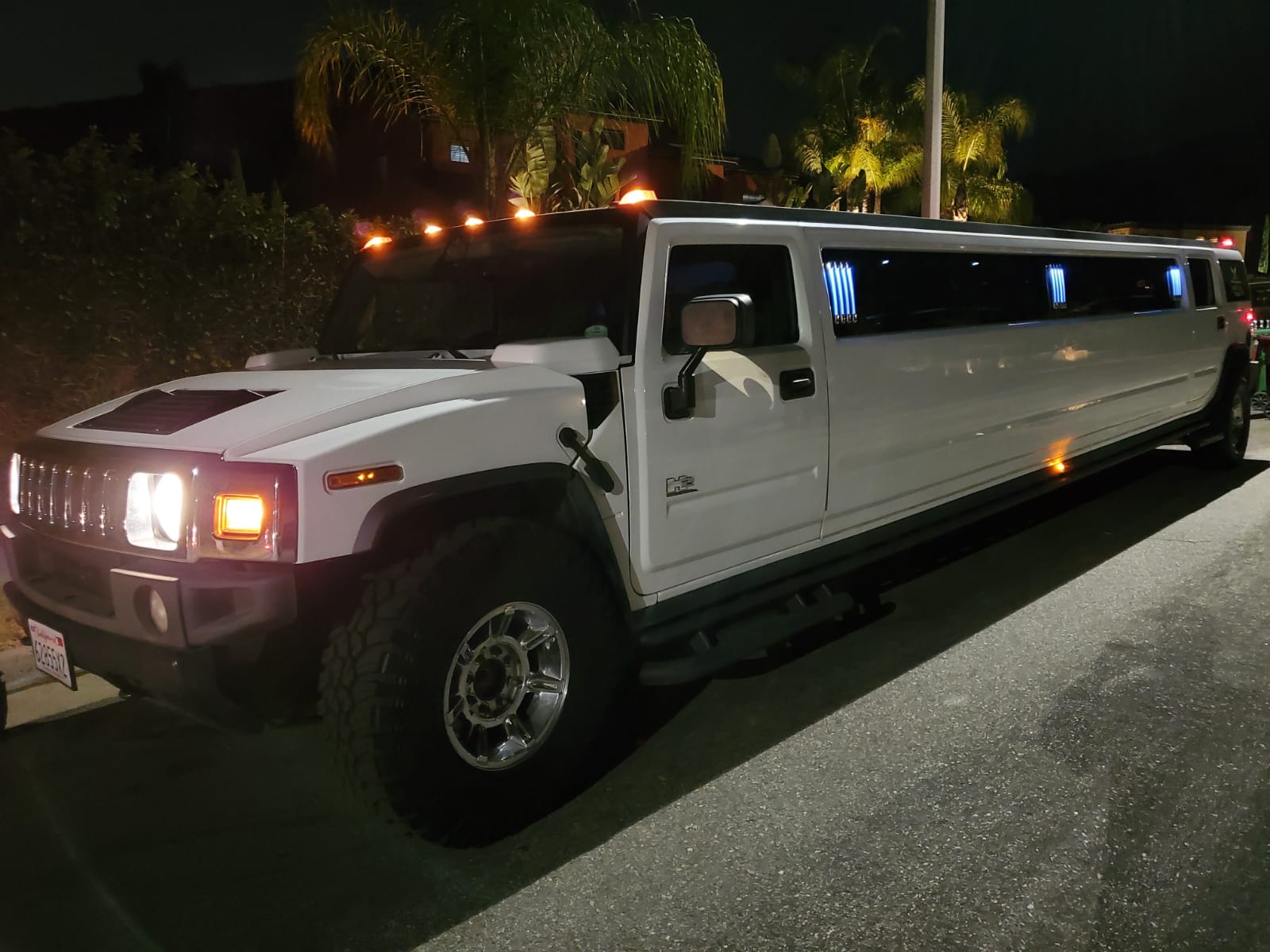 A white hummer limousine is parked on the side of the road at night.