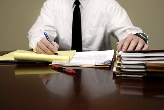 Un uomo elaborando il progetto di un documento e al suo fianco , vari documenti e cartelle impilati