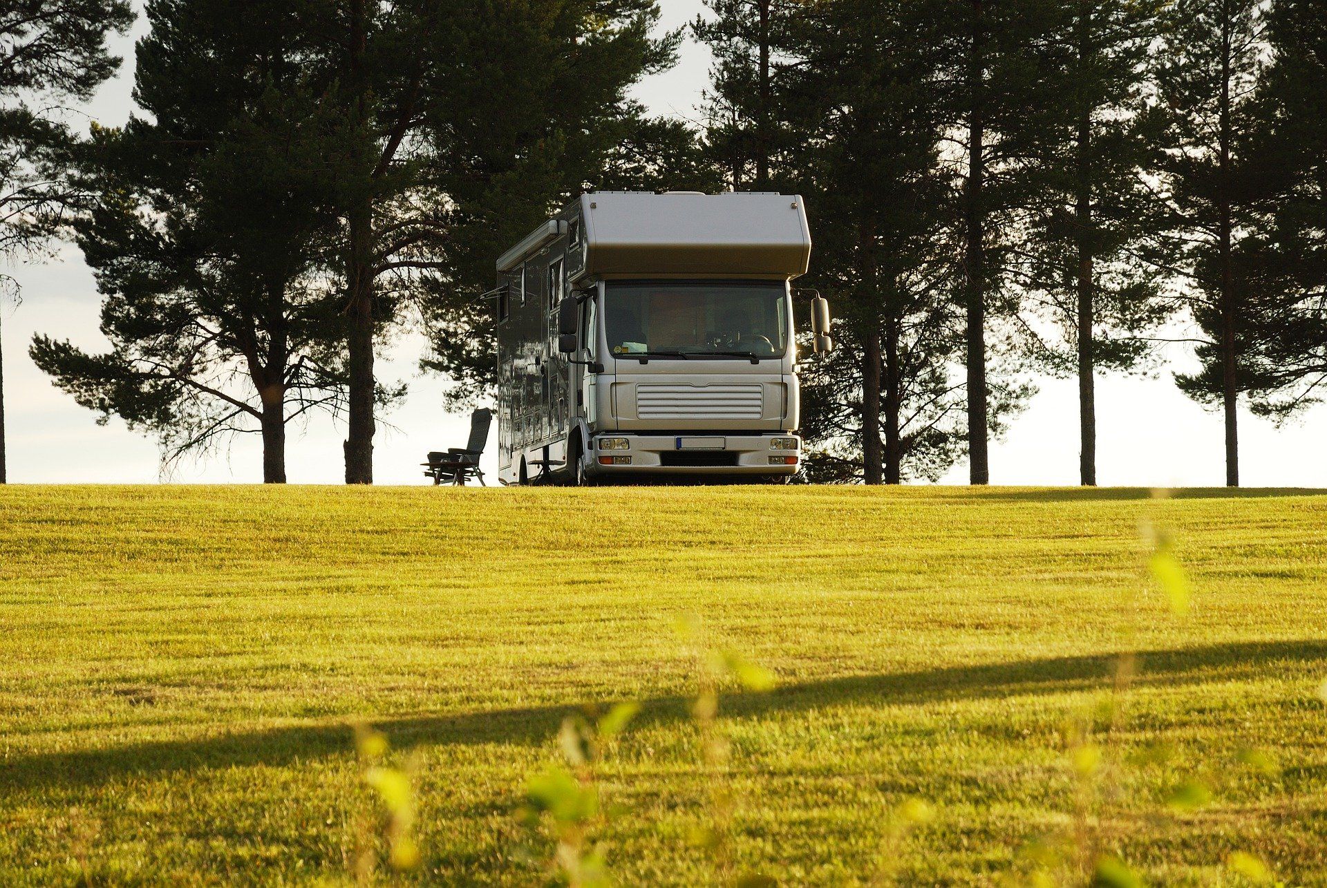 RV parked on a grassy hill, with trees in the background. Sunny outdoor setting.