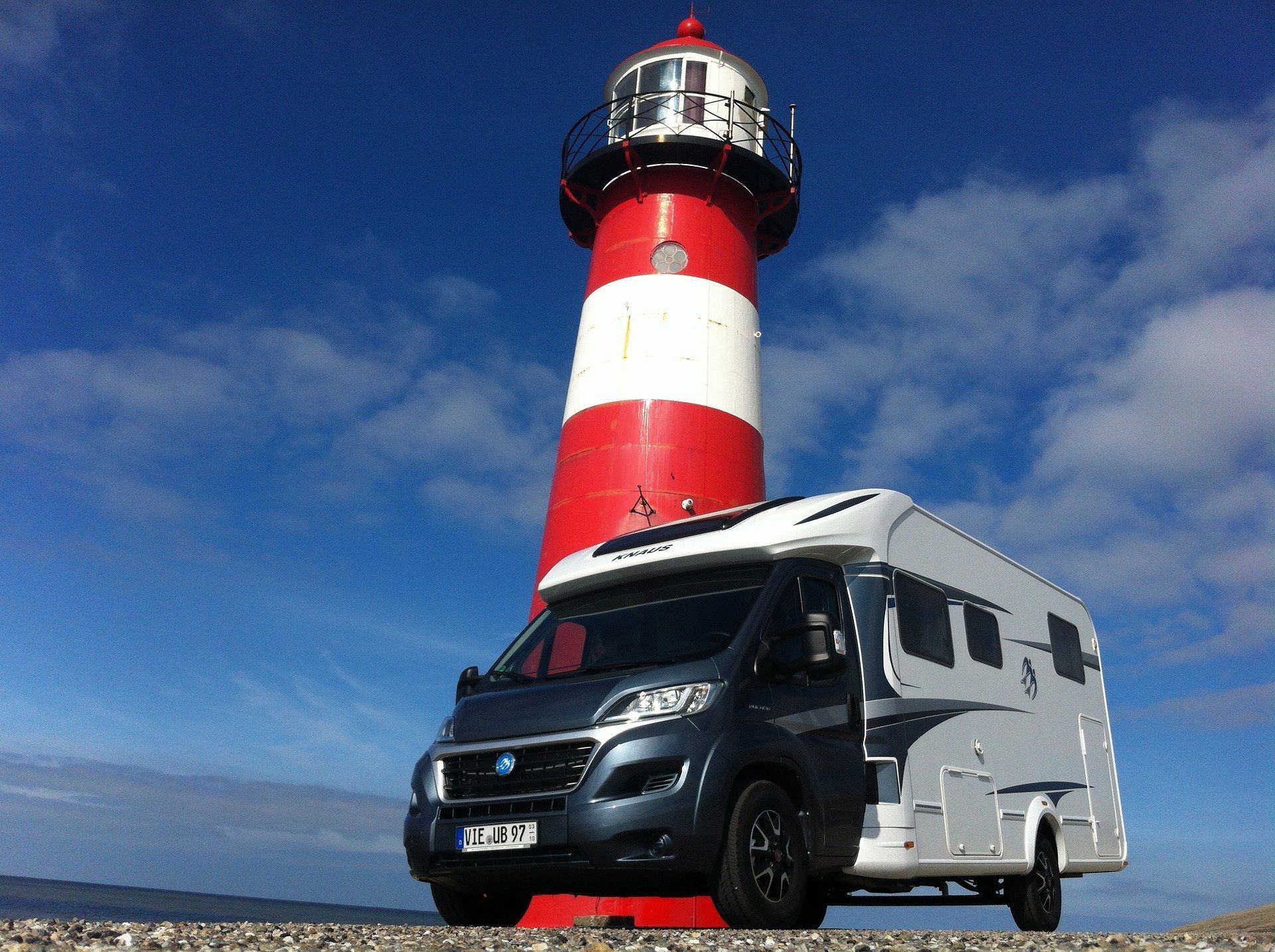 Motorhome parked next to a red and white striped lighthouse on a sunny day.