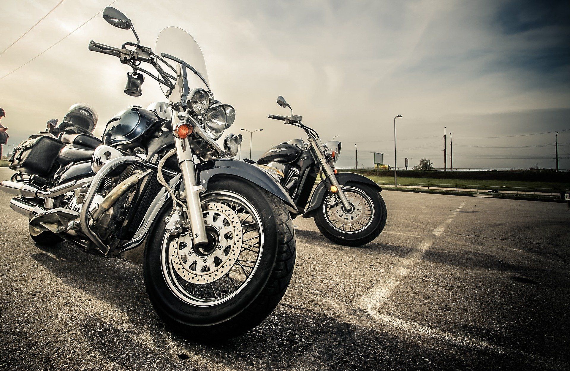 Two parked motorcycles on an asphalt surface under a cloudy sky. One has a windshield.