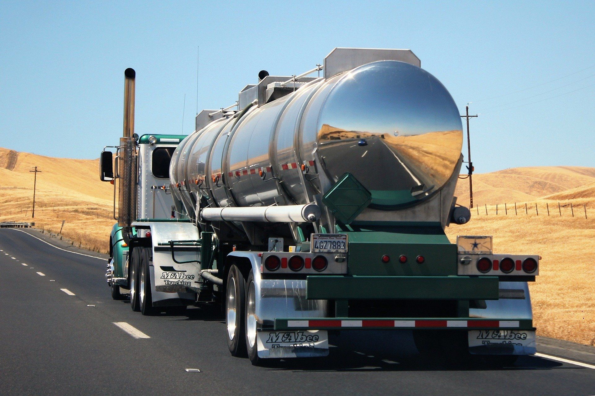 Tanker truck driving down a highway in a sunny, desert-like environment.