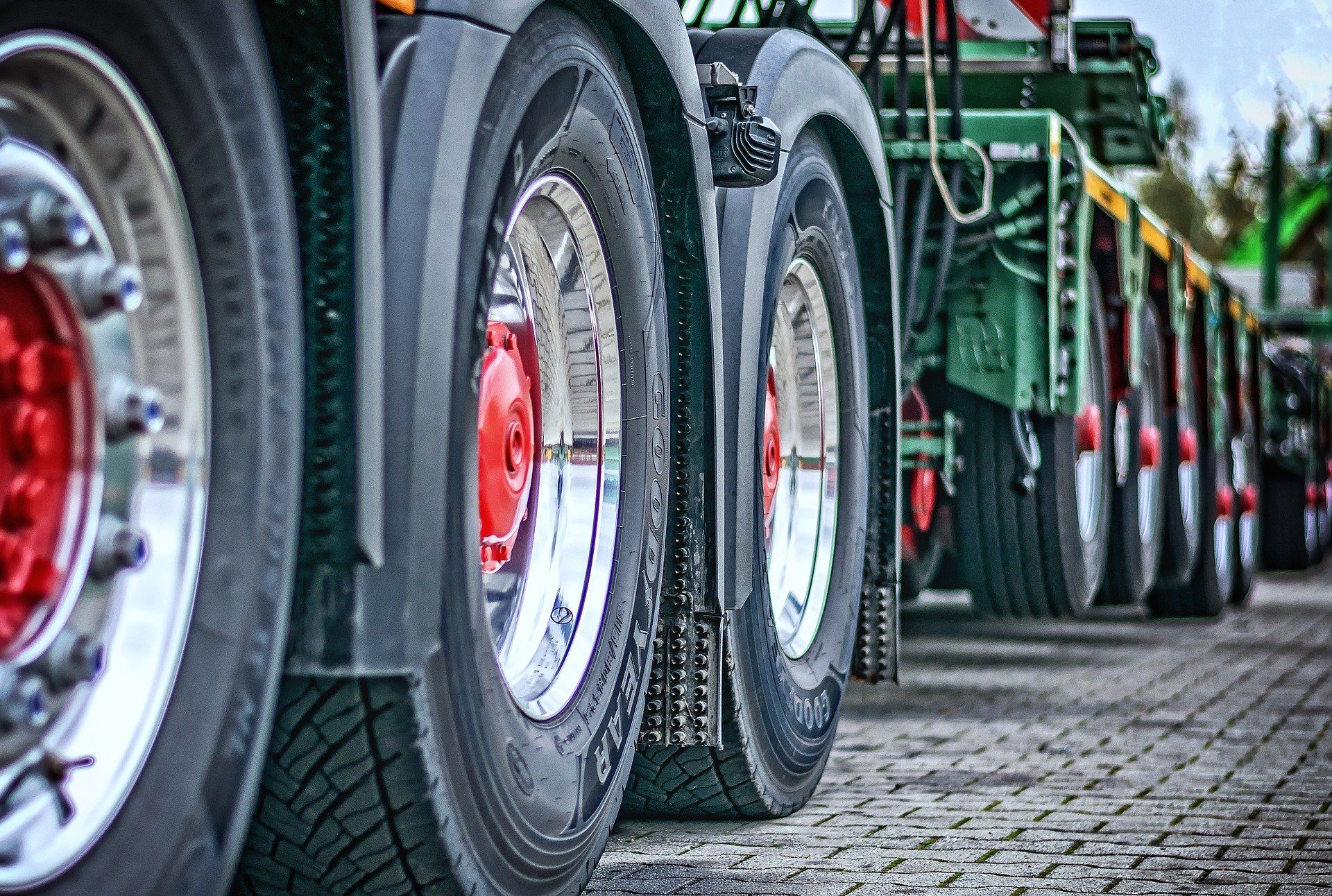 Close-up of several truck tires with shiny rims lined up on a cobblestone surface.