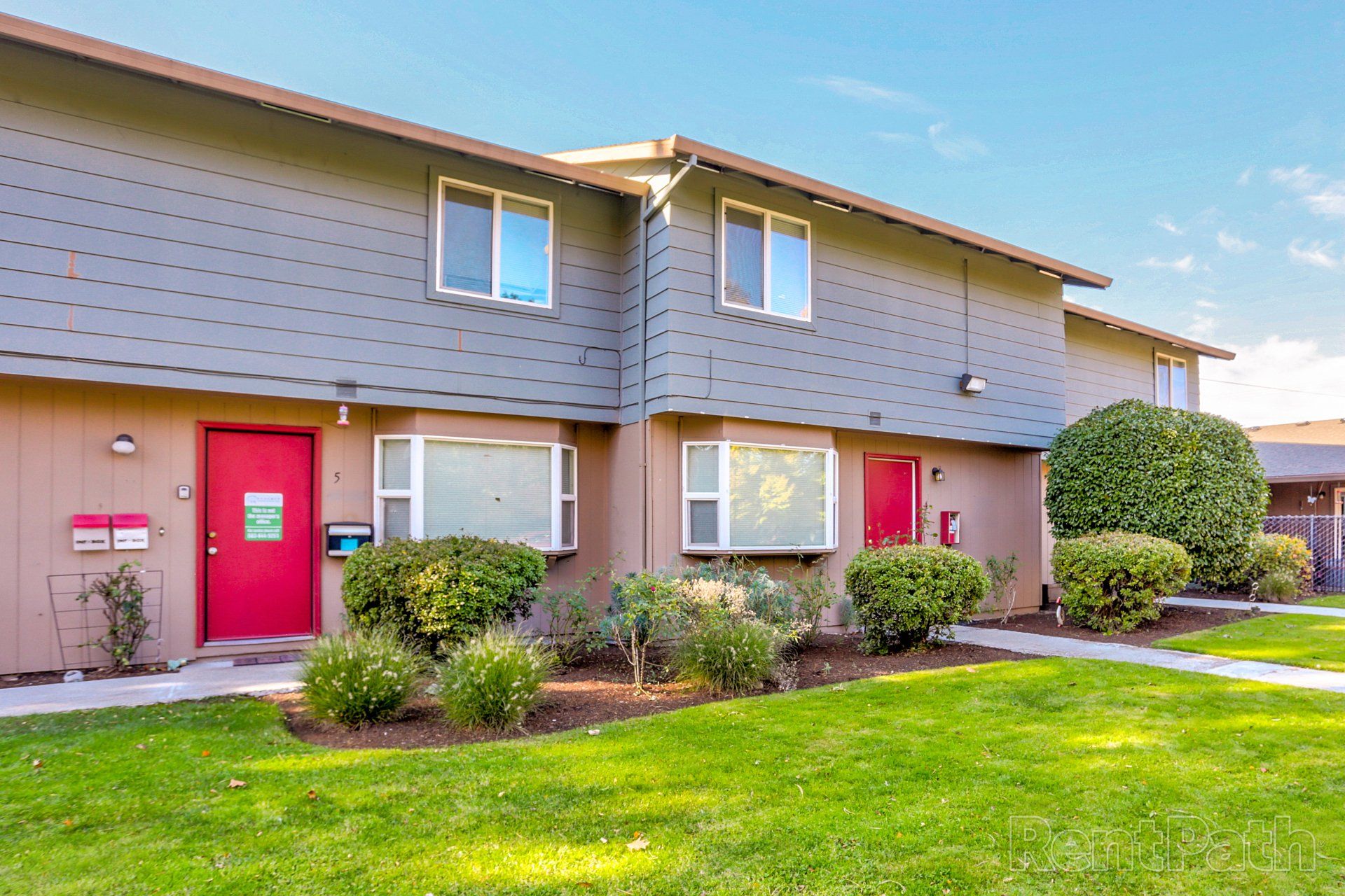 A house with a red door and a lush green lawn in front of it.